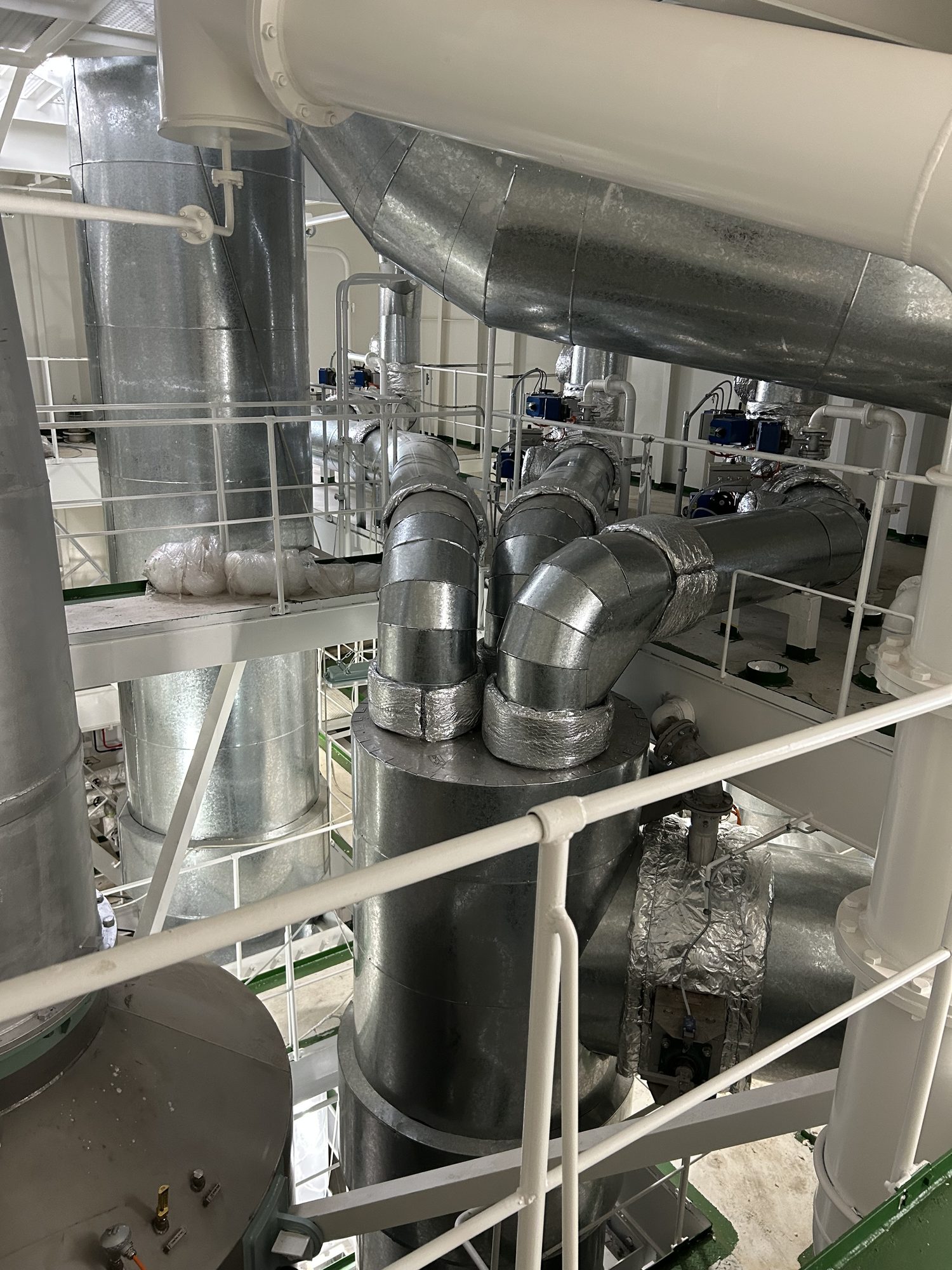 上から見下ろした設備区画。金属板で外装された太い配管や円筒形の機器が並んでいる
